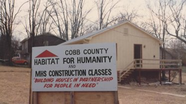 A picture of a sign that says "Cobb County Habitat for Humanity and MHS Construction Classes Building houses in partnership for people in need" posted in front of one of the first houses built by NW Metro Atlanta Habitat for Humanity.